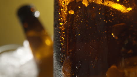 cerca de las gotas de condensación que corren por botellas de vidrio de cerveza fría o refrescos que se enfrían en un cubo lleno de hielo contra un fondo amarillo