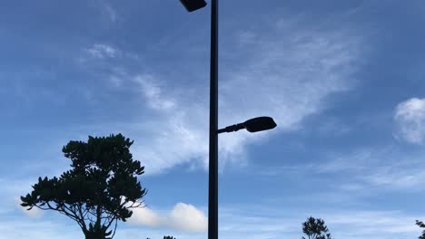 upward pan of a street light with two lamps in silhouette against a blue sky with wispy clouds