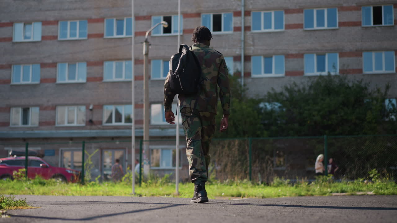 Soldier Walking Away, Soldier Moves Along Sunny Pathway, Military Personnel Departs Down Illuminated Street, Service Member Strides Toward Building Along Bright Sunlit Road With Back View