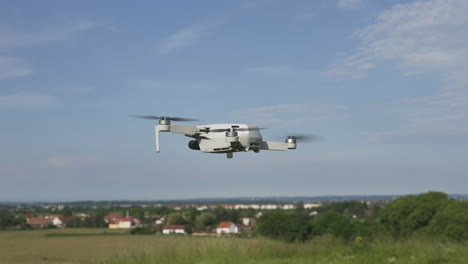 quadcopter consumer drone flying slowly above green suburban landscape on sunny day, slow motion