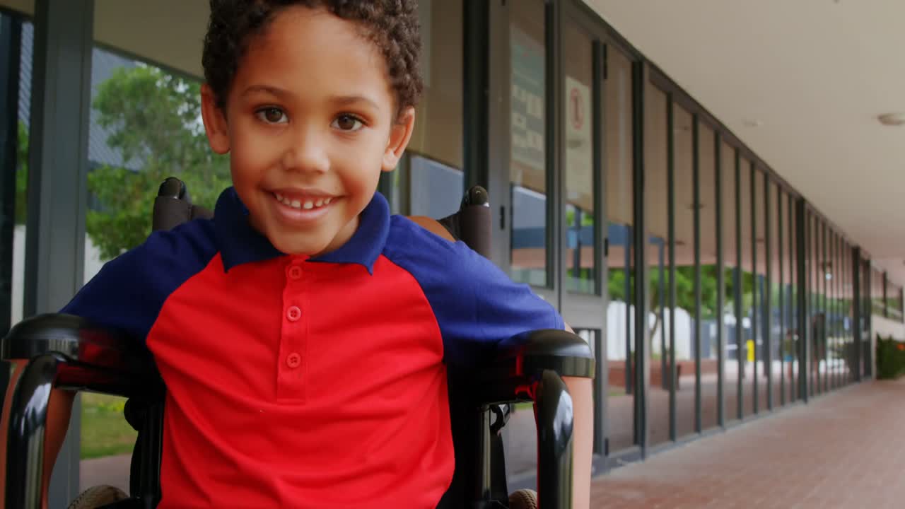 Front view of happy disabled African American schoolboy sitting on wheelchair in school corridor 4k