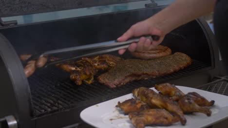 man moves bbq chicken thighs and sausage around on smoking bbq pit