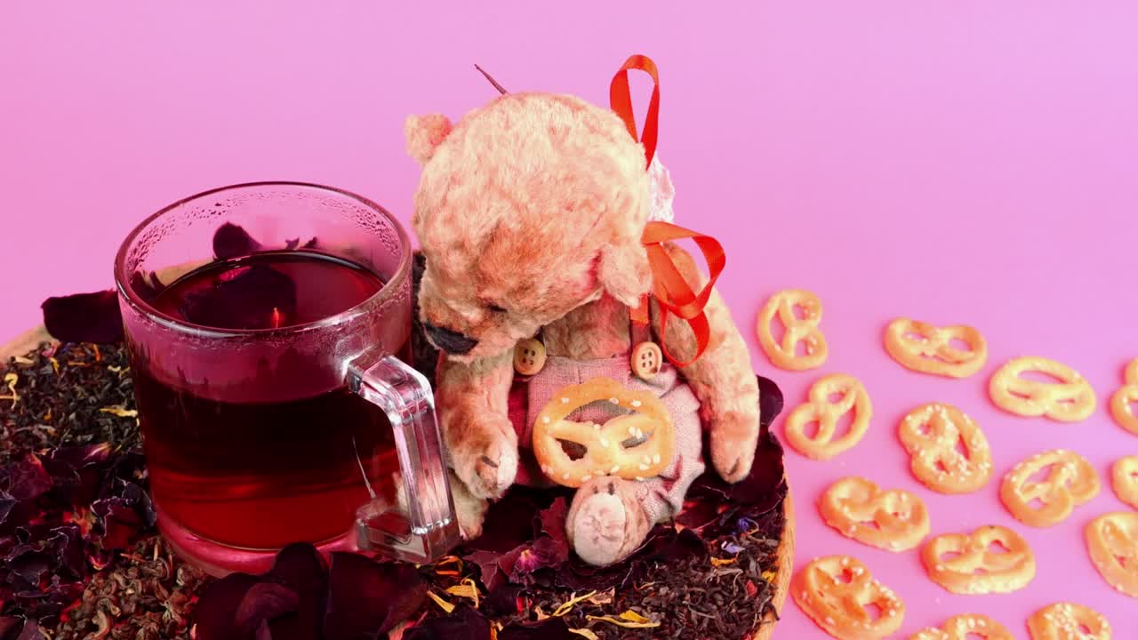 유리 컵에 꽃 차와 테디 베어는 분홍색 배경에 분홍색 조명으로 천천히 회전합니다.