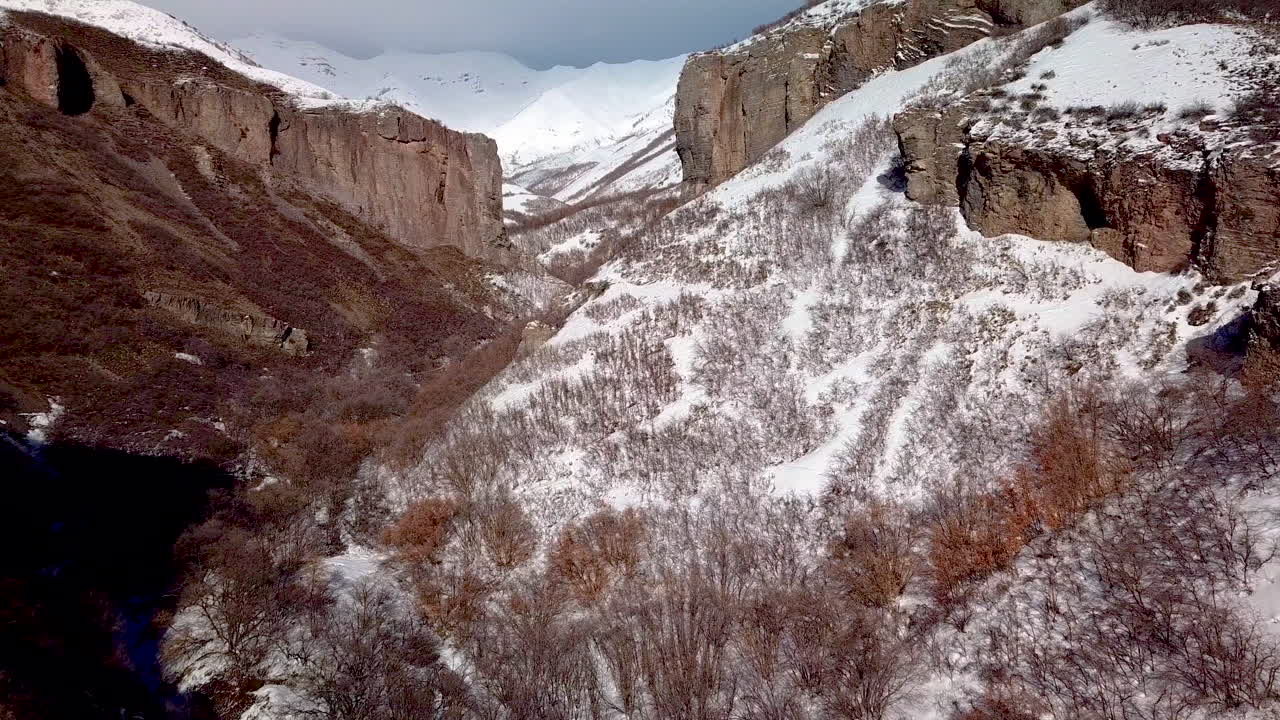 vista aérea del terreno accidentado con acantilados y montañas cubiertas de nieve por delante