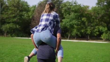 Back-view-of-a-young-african-guy-piggybacking-his-caucasian-happy-girlfriend-in-a-sunny-park.-Romantic-date-of-a-happy