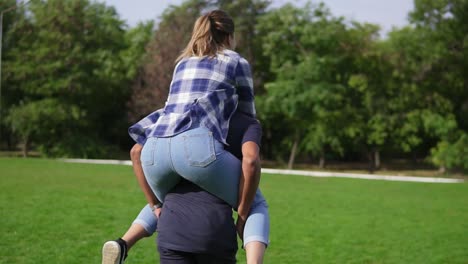 back view of a young african guy piggybacking his caucasian happy girlfriend in a sunny park. romantic date of a happy