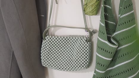 stylish light green beaded handbag hanging on a wall with other green garments