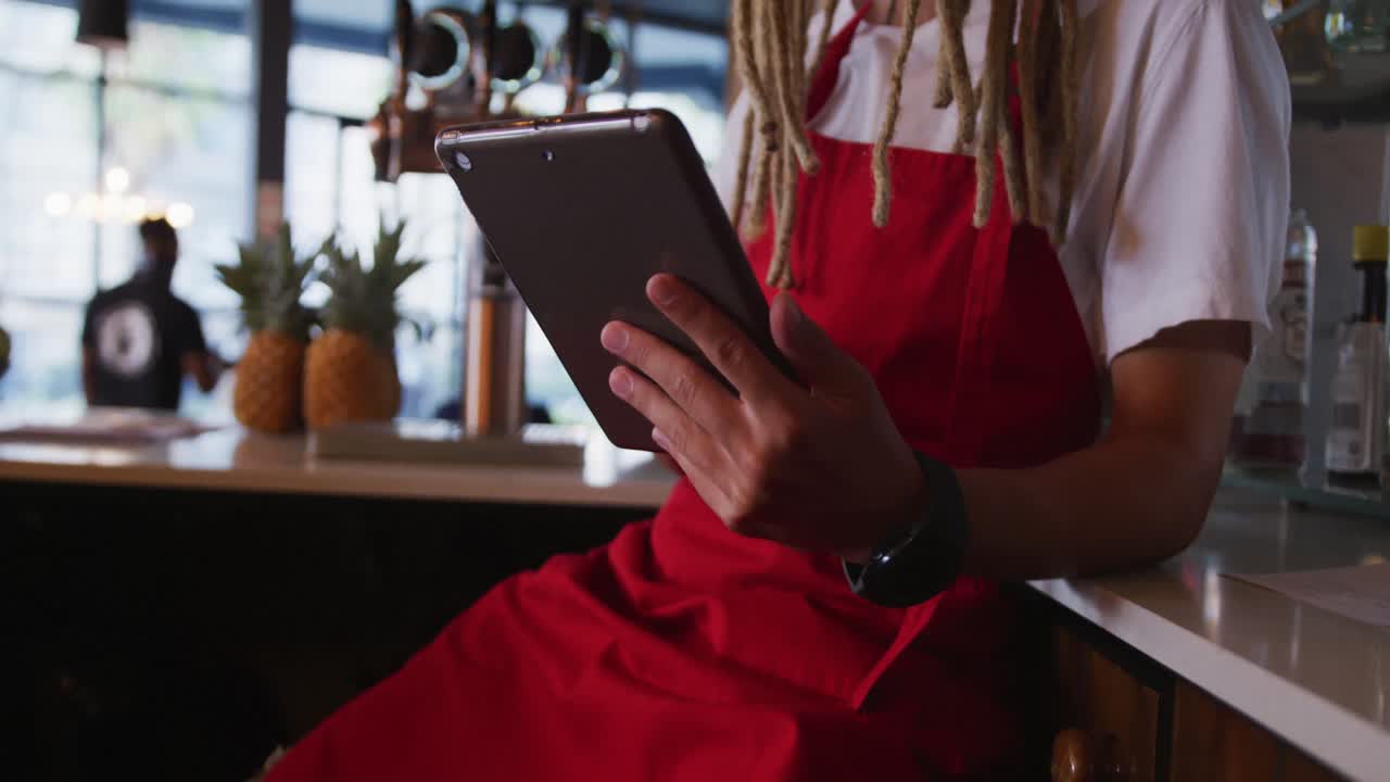 barista masculino de raza mixta con rastas con un delantal usando una tableta digital