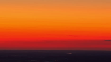 a stunning view of a sunset sky with a beautiful, smooth gradient from deep red to vibrant orange, with the tiny silhouette of a distant airplane flying across the colorful horizon.