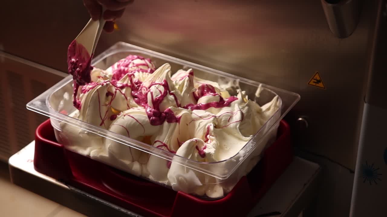 Mano che cola salsa magenta su gelato bianco.