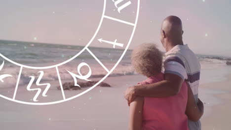 animation of horoscope moving over happy senior african american couple embracing at beach