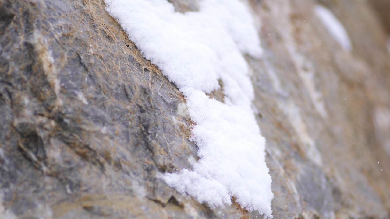 Leichter Schnee fällt auf eine strukturierte Felsoberfläche