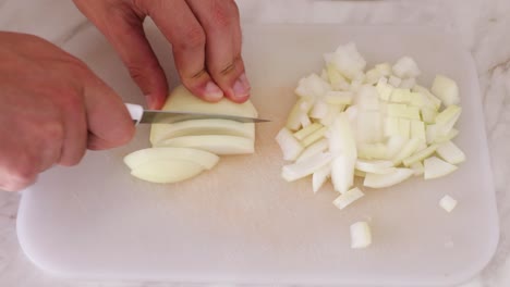 closeup of a mans hand cutting up the onions on a white board with a steel knife