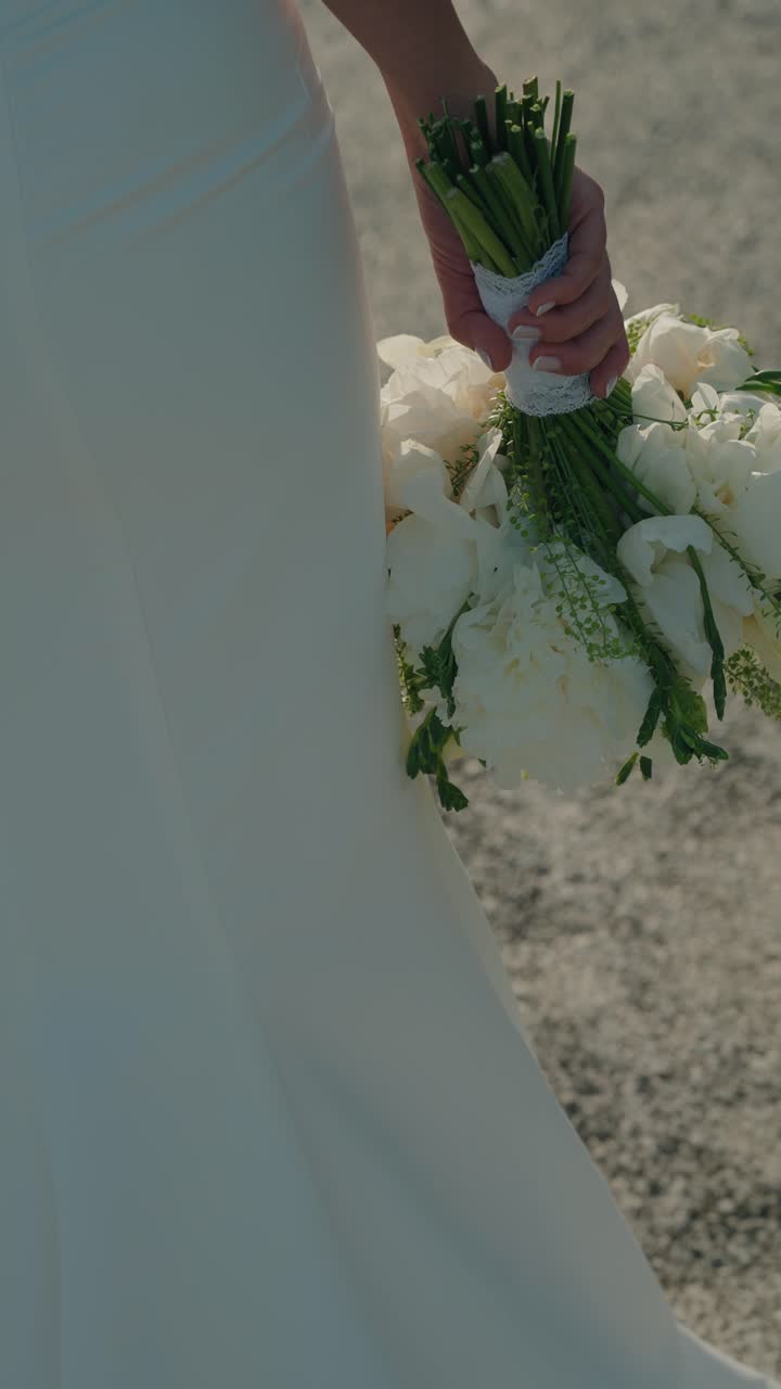 Primo piano verticale della mano della sposa che tiene fiori bianchi.