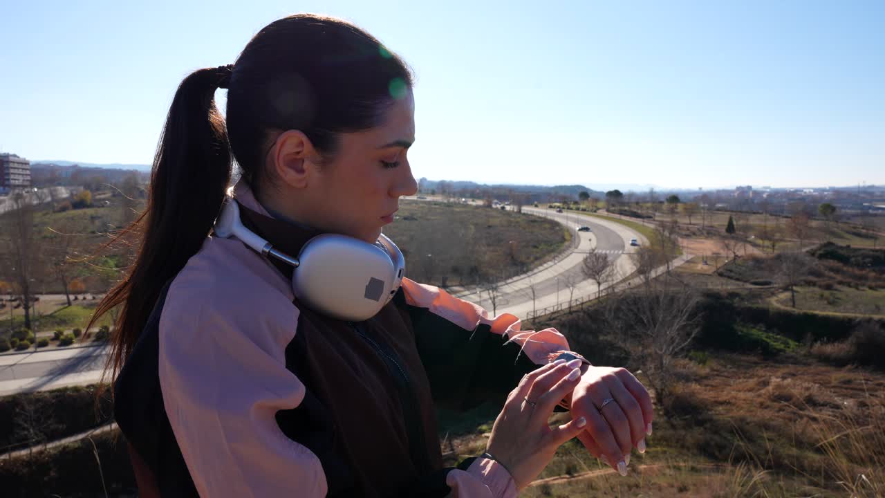 Corridore controlla le statistiche dello smartwatch su una collina con uno sfondo di campagna soleggiata
