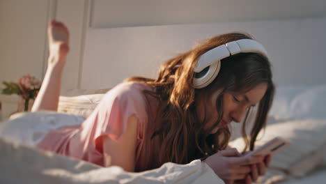 home girl listening headphones in sunlight closeup. carefree model lying bed