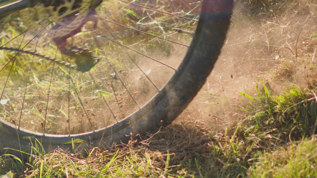 Close Up Slow Motion of Bicycle Rolling Down Dry Grass and Kicking Up Dirt as it Rolls By. Golde Hour Lighting with Tyres and Spokes Visible on Bike. Exercise Sports Clip.