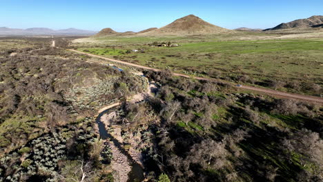 Aerial-shot-of-car-driving-on-dirt-road-in-Willcox,-Arizona,-wide-rotating-side-angle-drone-shot-with-mountains-in-the-background