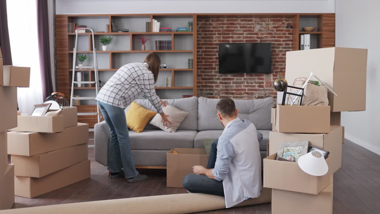 젊은 부부는 이동하는 날에 새로운 아파트에서 카드보드 상자를 열고 인테리어 디자인을 논의합니다. 이주하는 날 행복한 주택 소유자. 부동산 및 임대 개념. 젊은 가족을위한 대출 모기지.