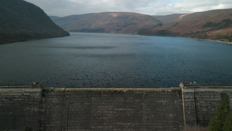 flying towards and over reservoir dam wall to windswept lake of haweswater english lake district uk