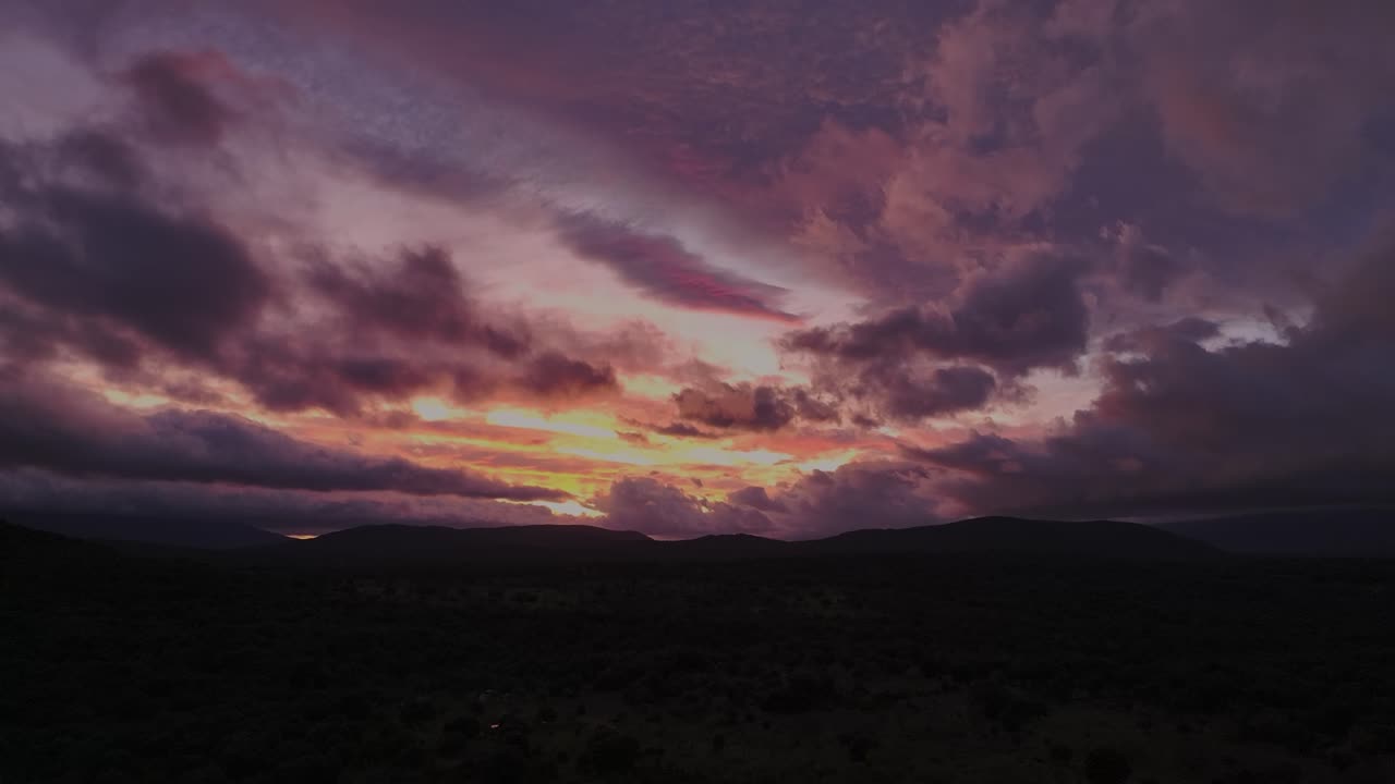 Ascending sunset shot with bright purple, orange, and gray cumulus and cirrus clouds over a mountain valley fading into twilight.