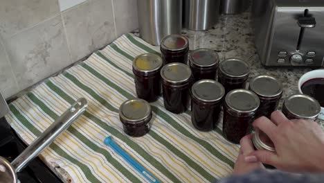 putting the lids and seals on fresh homemade jars of berry jam - over-the-shoulder view