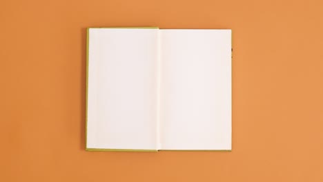 green vintage hardcover book appear and open with copy space on orange background. stop motion flat lay