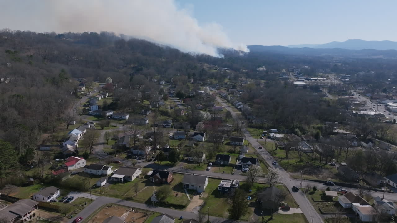Aerial drone footage flying over a neighborhood in Rossville, Georgia that pans up to reveal a forest fire in the background.