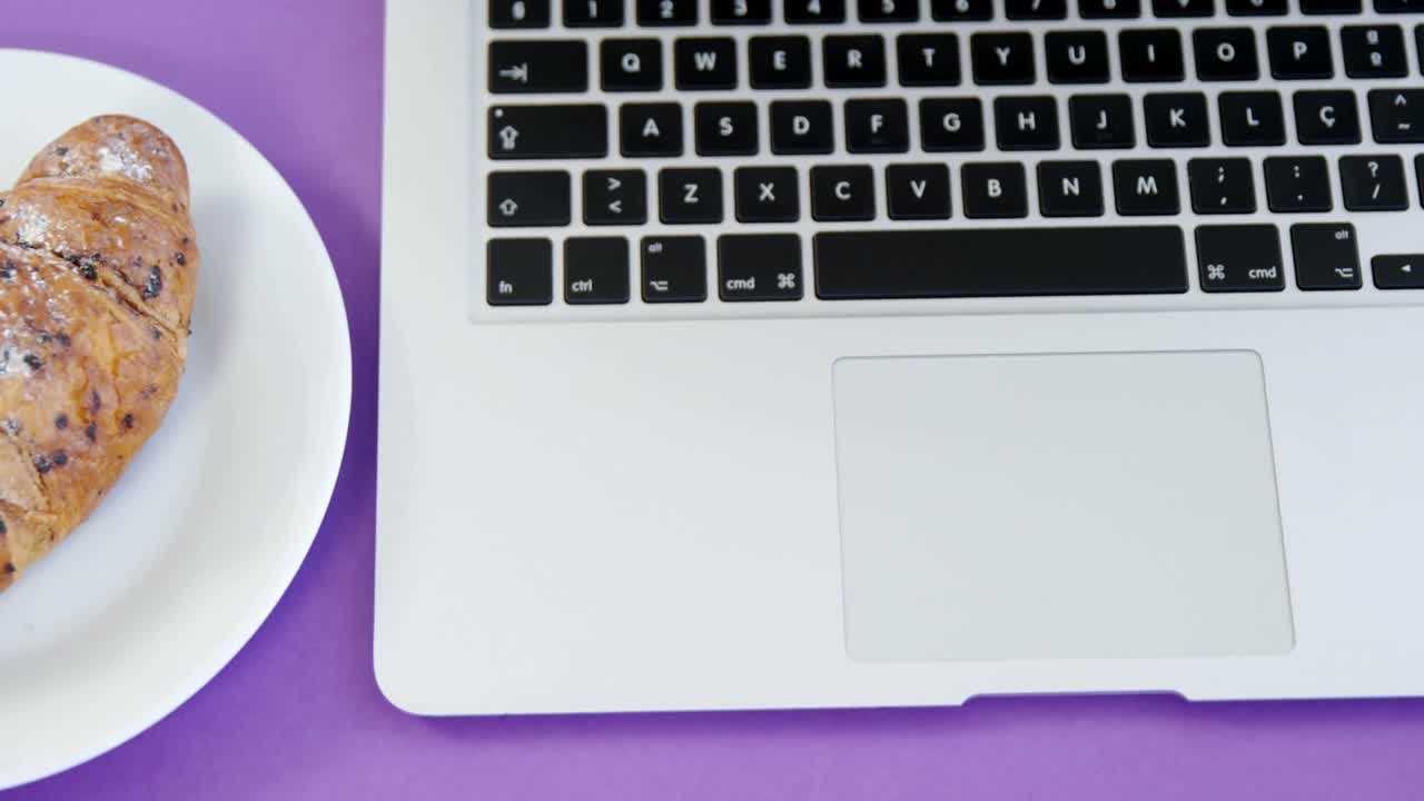 croissant y portátil en fondo púrpura 4k