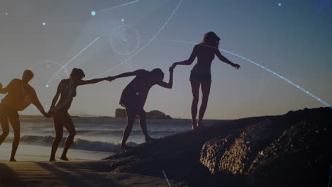 animación de una red de comunicación brillante sobre amigas tomadas de la mano caminando por la playa al atardecer