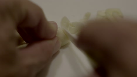 close up hand cutting garlic with small kitchen knife on cutting board