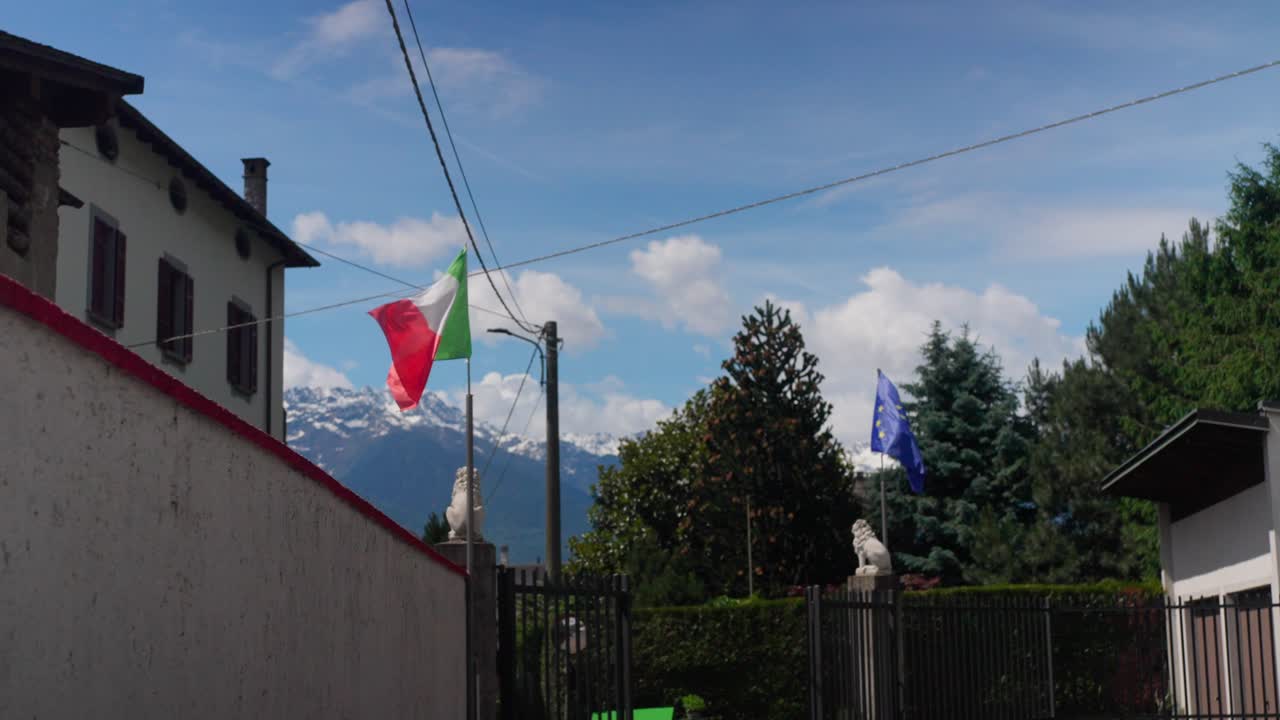 Bandiera nazionale italiana e bandiera dell'Unione Europea che sventolano al vento sullo sfondo di montagne innevate.