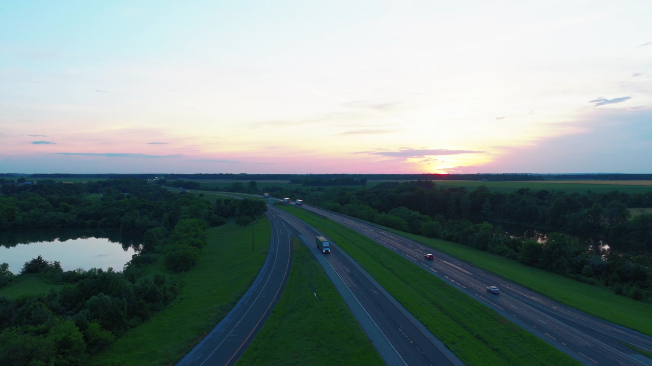 Jalan Tol Antar Negara Bagian 64 membentang menuju matahari terbenam merah muda dekat Richview, Illinois, sebuah jalan raya terpisah dan danau di tepi jalan bersinar dalam cahaya senja musim panas yang hangat