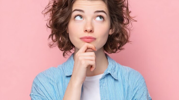 Una donna pensierosa con capelli ricci e un'espressione contemplativa guarda in alto, riflettendo sulla sua prossima mossa su uno sfondo rosa vibrante