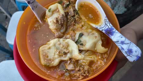 top down shot over a plate of steamed momo with soup served in a yellow bowl been served at a roadside food stall