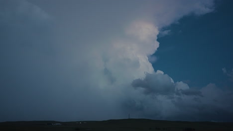 lightning flashes in a towering storm cloud in soft dusk light