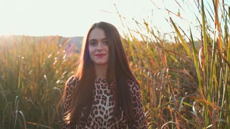 Young-Caucasian-pretty-brunette-woman-walking-in-tall-green-grass-field-towards-camera-on-bright-sunny-day,-close-up-portrait-slow-motion