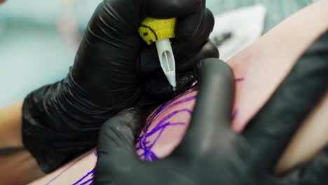 making tattoo with a special ink machine device. tattoo professional in black gloves puts ink on the sketch lines. close up.