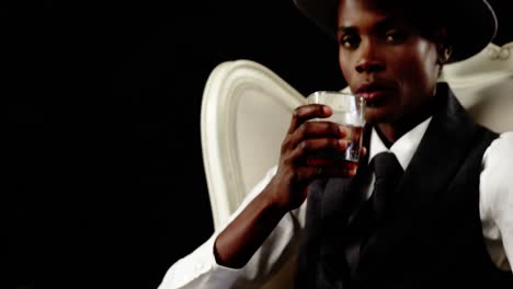 androgynous man drinking whisky on armchair