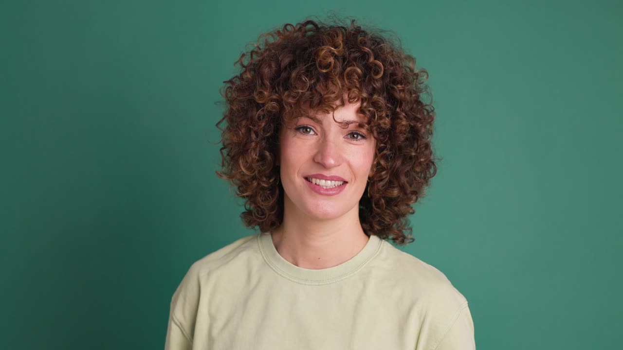 Smiling standing young curly haired woman on green background
