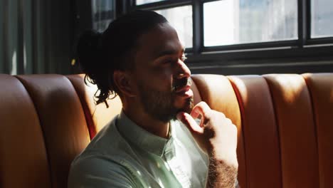 Mixed-race-man-sitting-in-cafe-looking-at-window-and-smiling