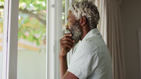 Portrait-of-african-american-senior-man-with-beard-looking-out-of-window-and-thinking