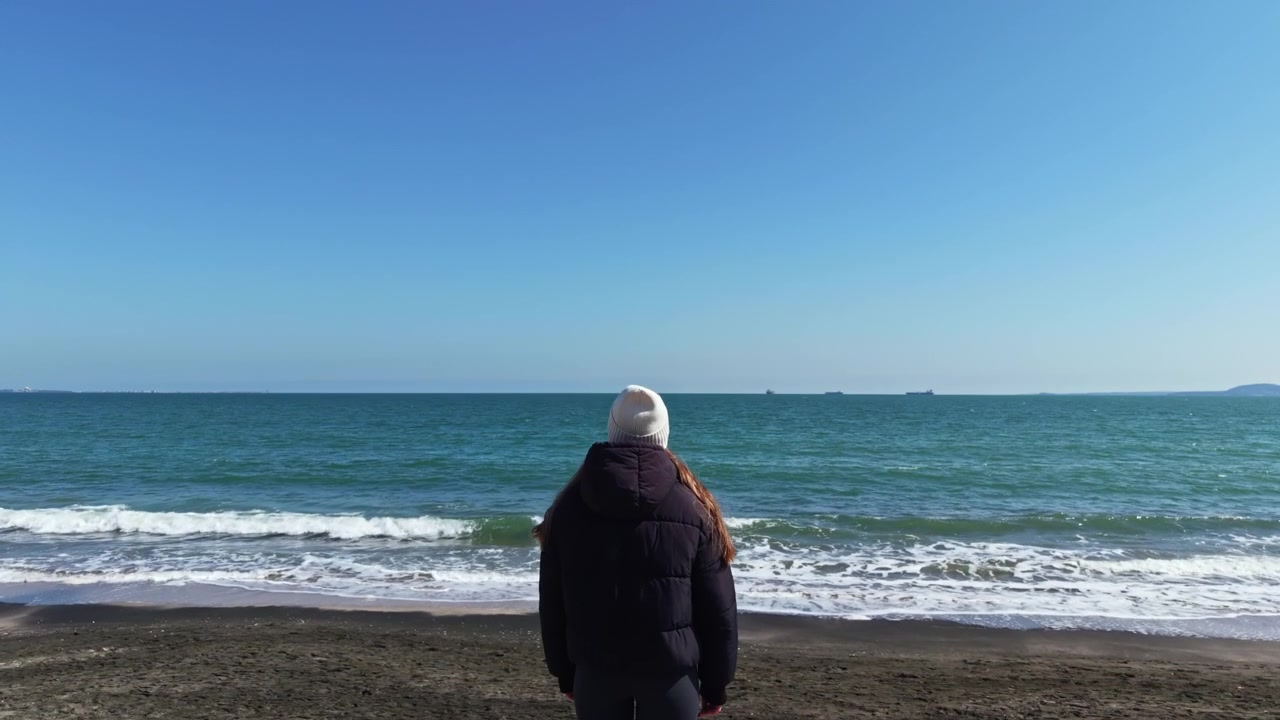 穏やかな冬の日の午後、ビーチに立つ人が、海と青い空を眺めています。