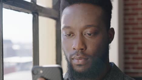 portrait young african american man using smartphone at home browsing messages networking texting social media sharing lifestyle online planning ahead in modern apartment close up