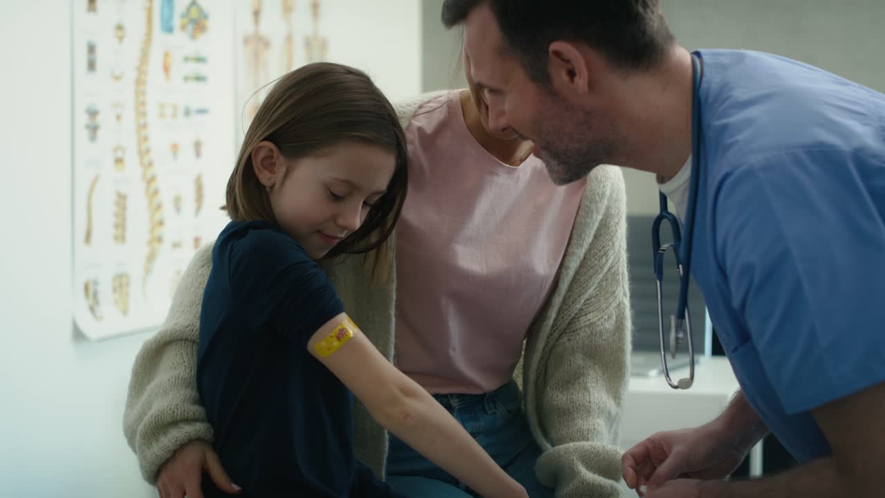 un médico general caucásico alegre le da a una chica una piruleta como premio después de la vacunación