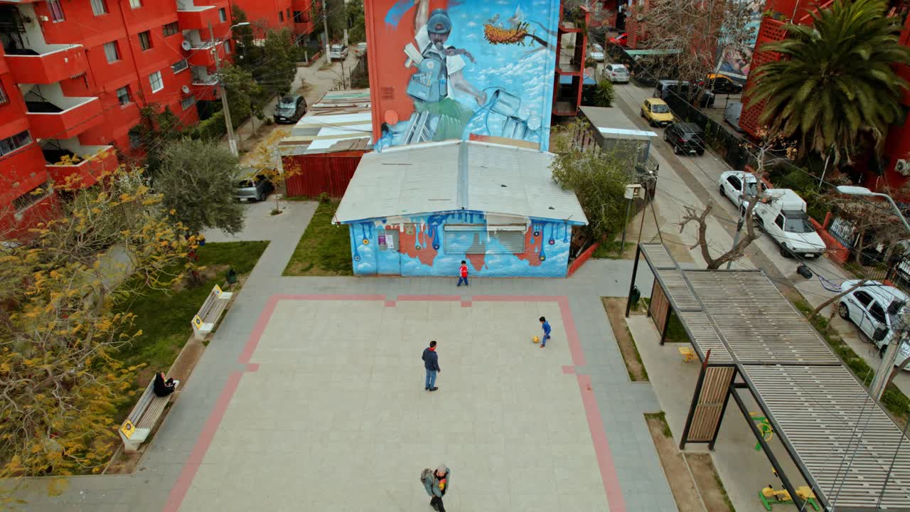 Drone tilt down shot of children playing soccer with adults in the open air museum in San Miguel, a reclaimed residential neighborhood. Santiago de Chile