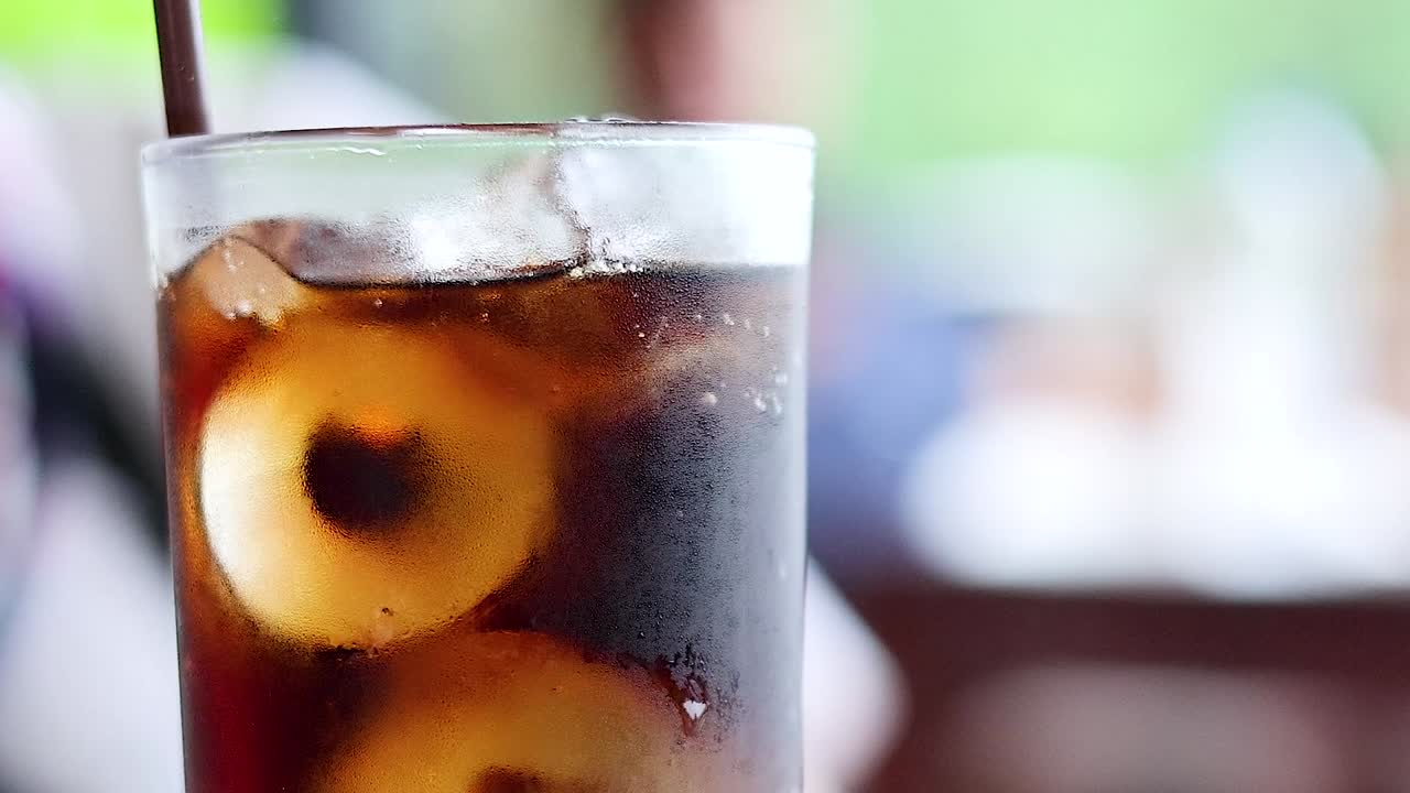 Primo piano di una cola fredda con cubetti di ghiaccio e una cannuccia