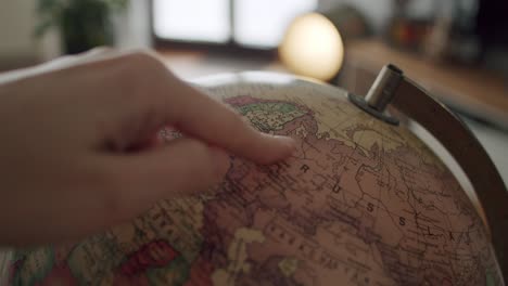 Close-up-shot-of-a-globe-spinning-until-a-hand-enters-frame-and-points-at-Russia