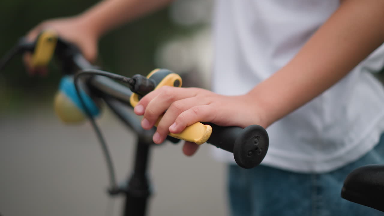 자전거의 손잡이에 노란색 브레이크 레버를 잡고 있는 작은 소년의 손의 클로즈업