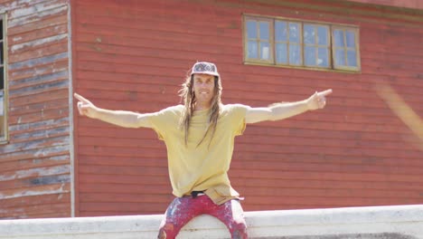 Video-portrait-of-happy-caucasian-male-artist-with-dreadlocks-sitting-on-wall-raising-hands